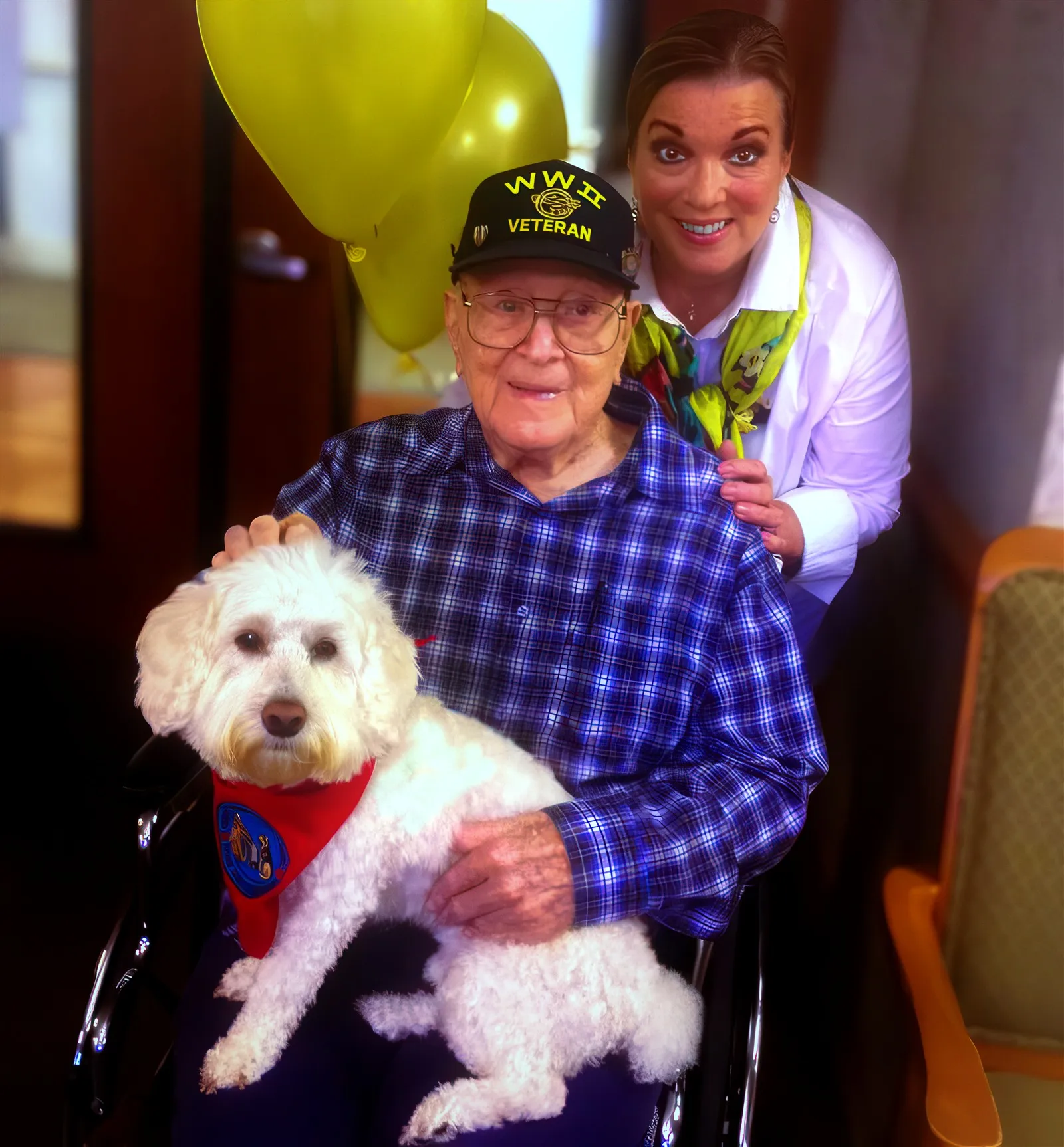 Jay R. Ricks in a WWII veteran cap and plaid shirt, a white dog on his lap, with his daughter Robyn Stewart leaning in behind him.