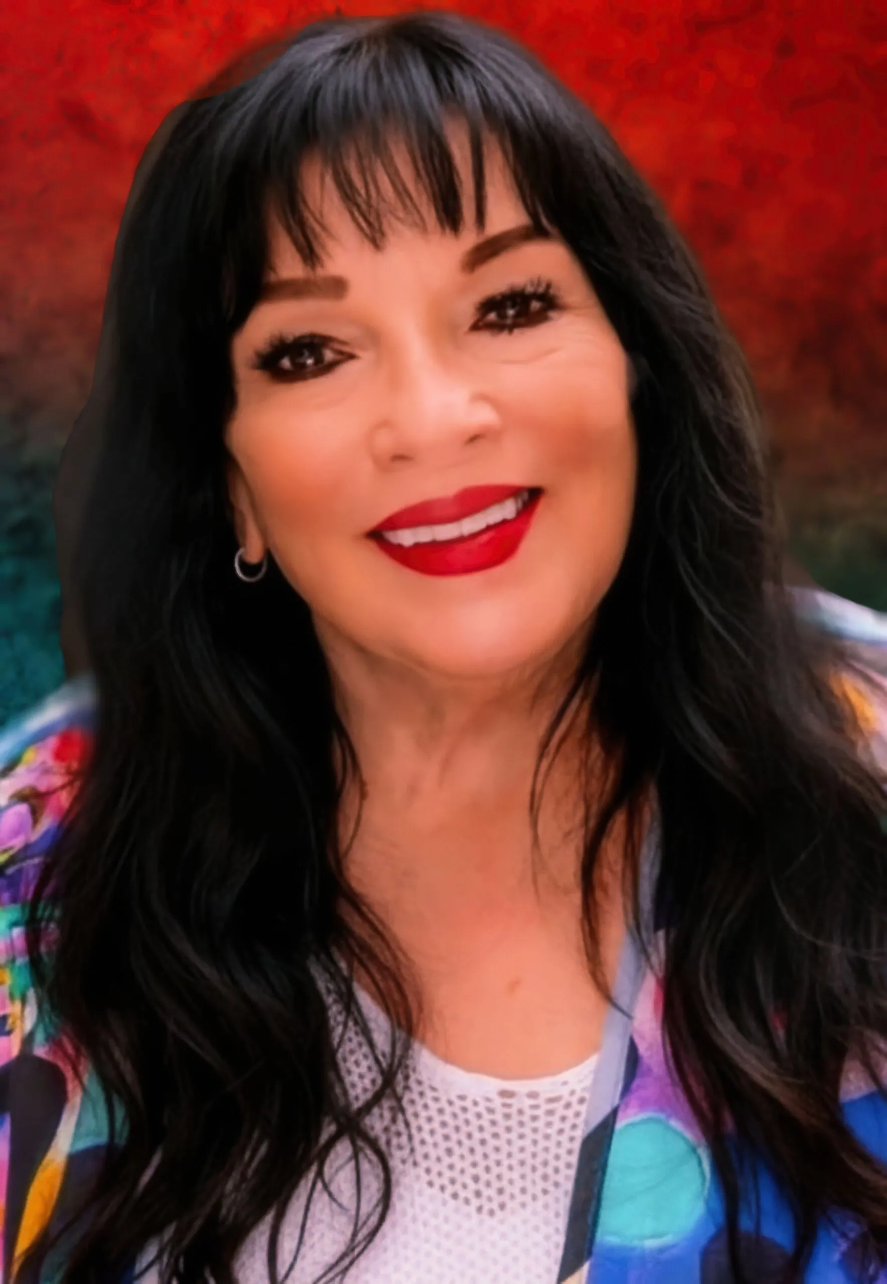Robyn Stewart smiling in a bright patterned jacket against a teal and orange backdrop (presskit precleared).